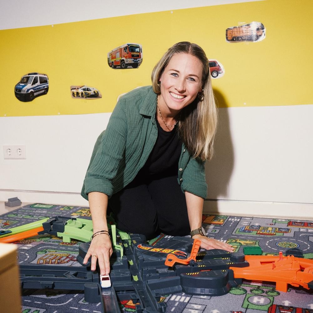 Foto: DIE KAVALLERIE GmbH Auf dem Foto spielt eine Frau auf einem Spiel-Straßen-Teppich und lacht dabei in die Kamera.
