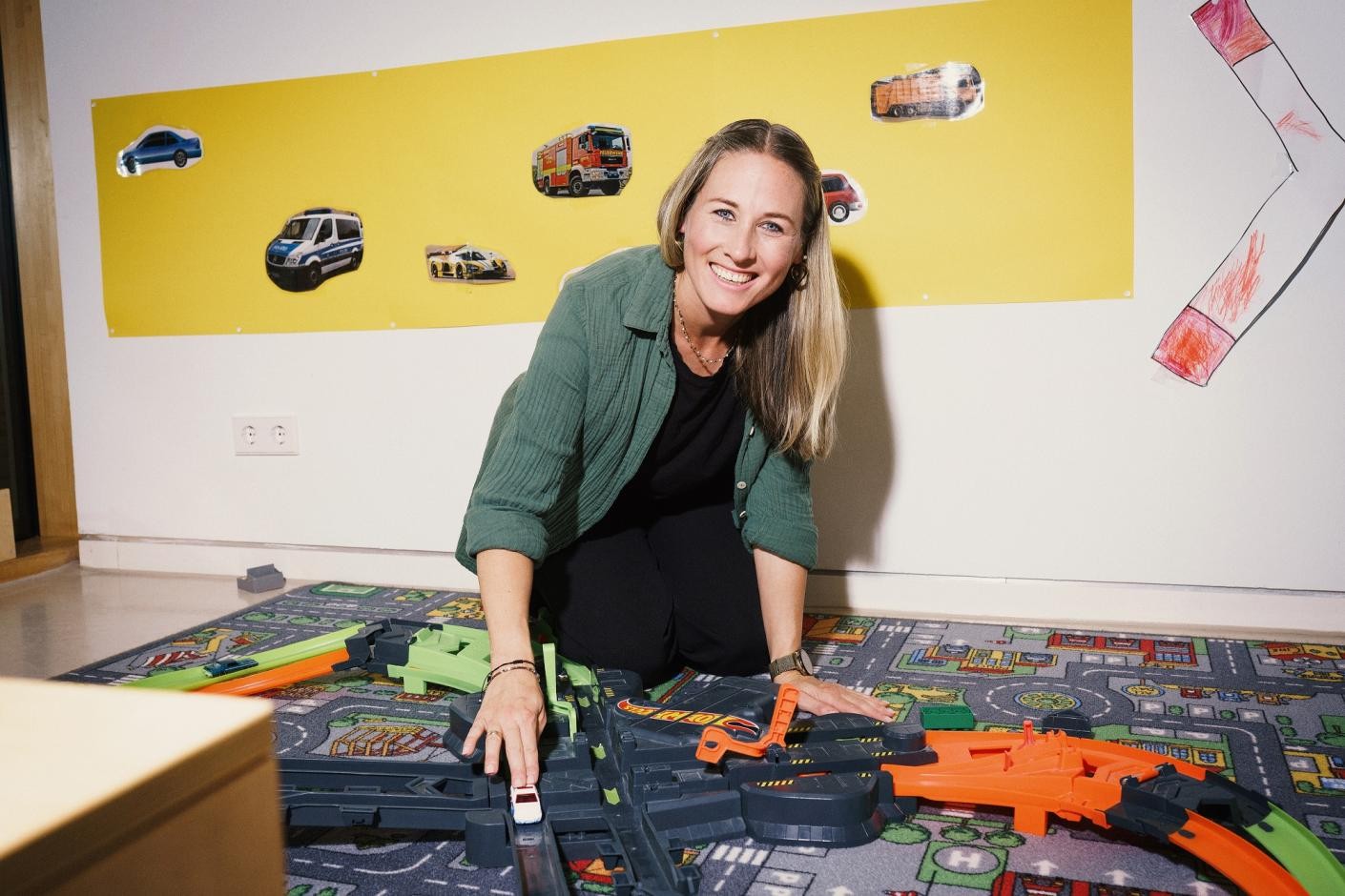 Foto: DIE KAVALLERIE GmbH Auf dem Foto spielt eine Frau auf einem Spiel-Straßen-Teppich und lacht dabei in die Kamera.